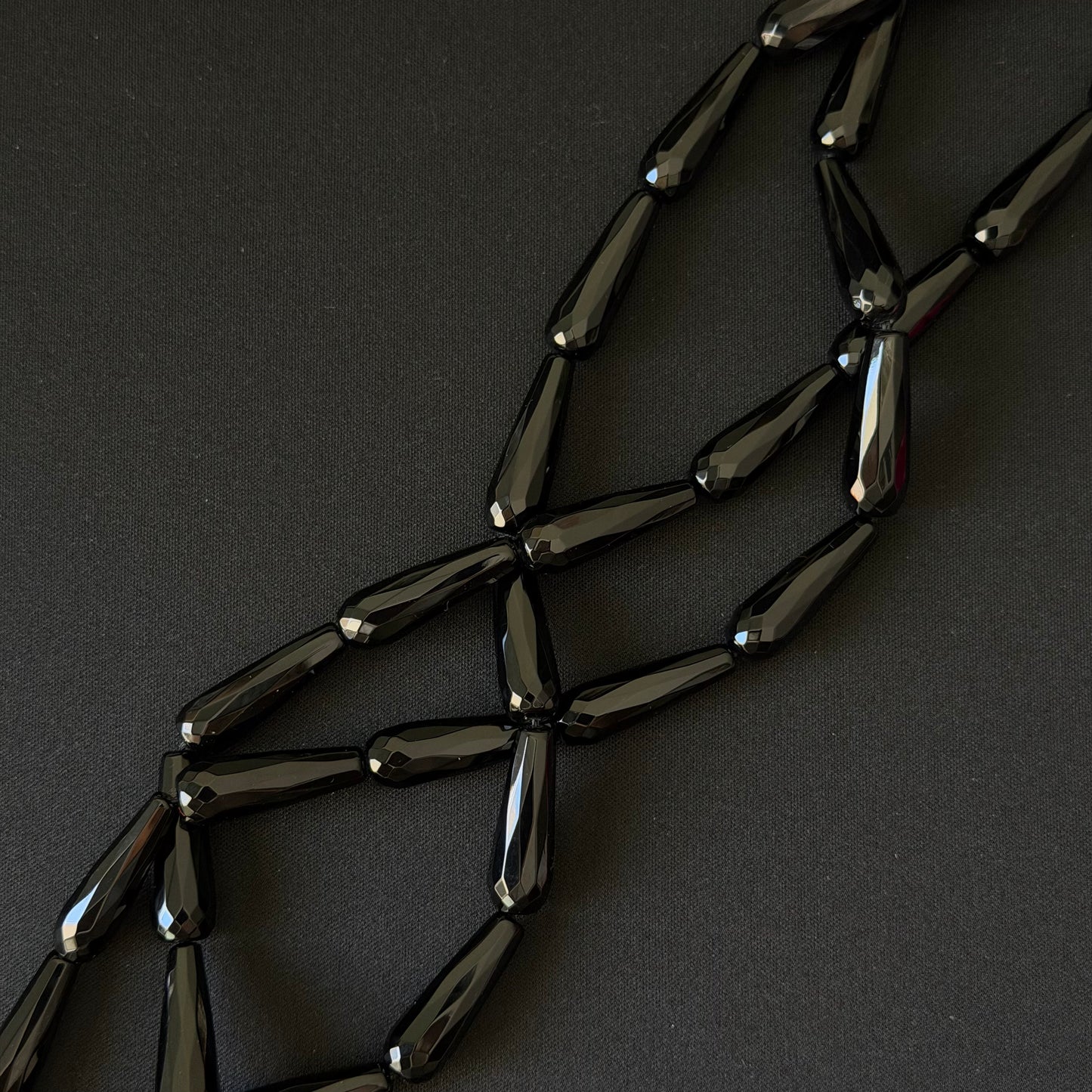 Black onyx teardrop beads on a string for necklace making, on a dark background
