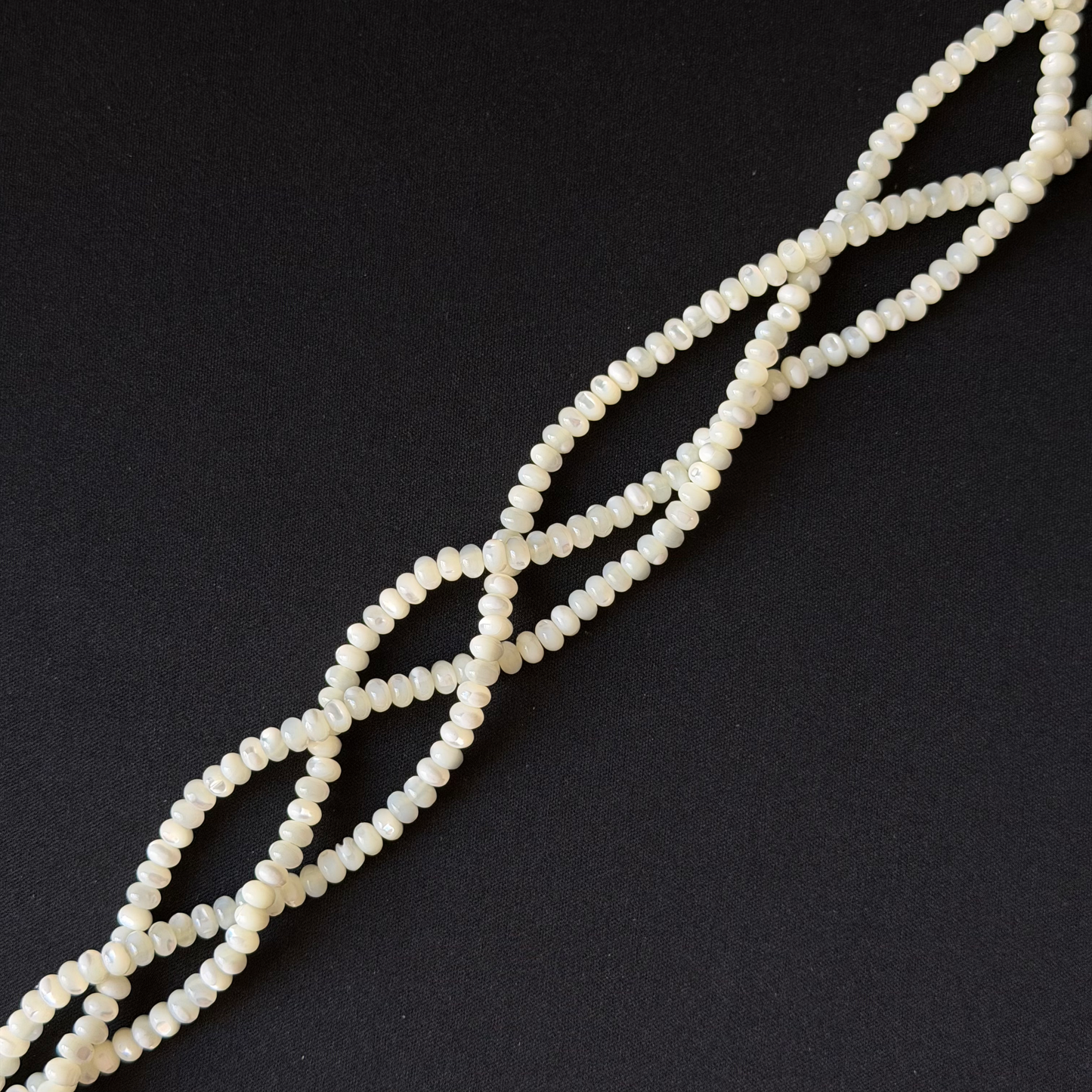 A strand of small, round, off-white beads arranged in a diagonal line on a solid black background.