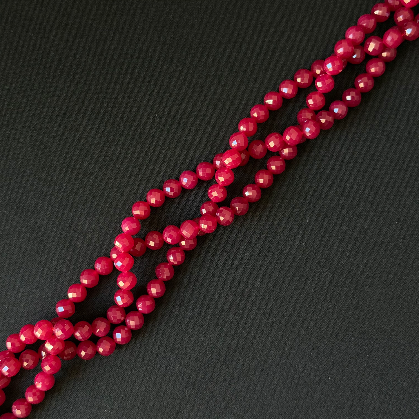 Faceted round beads in a deep berry pink color, arranged in diagonal strands on a dark textured background.