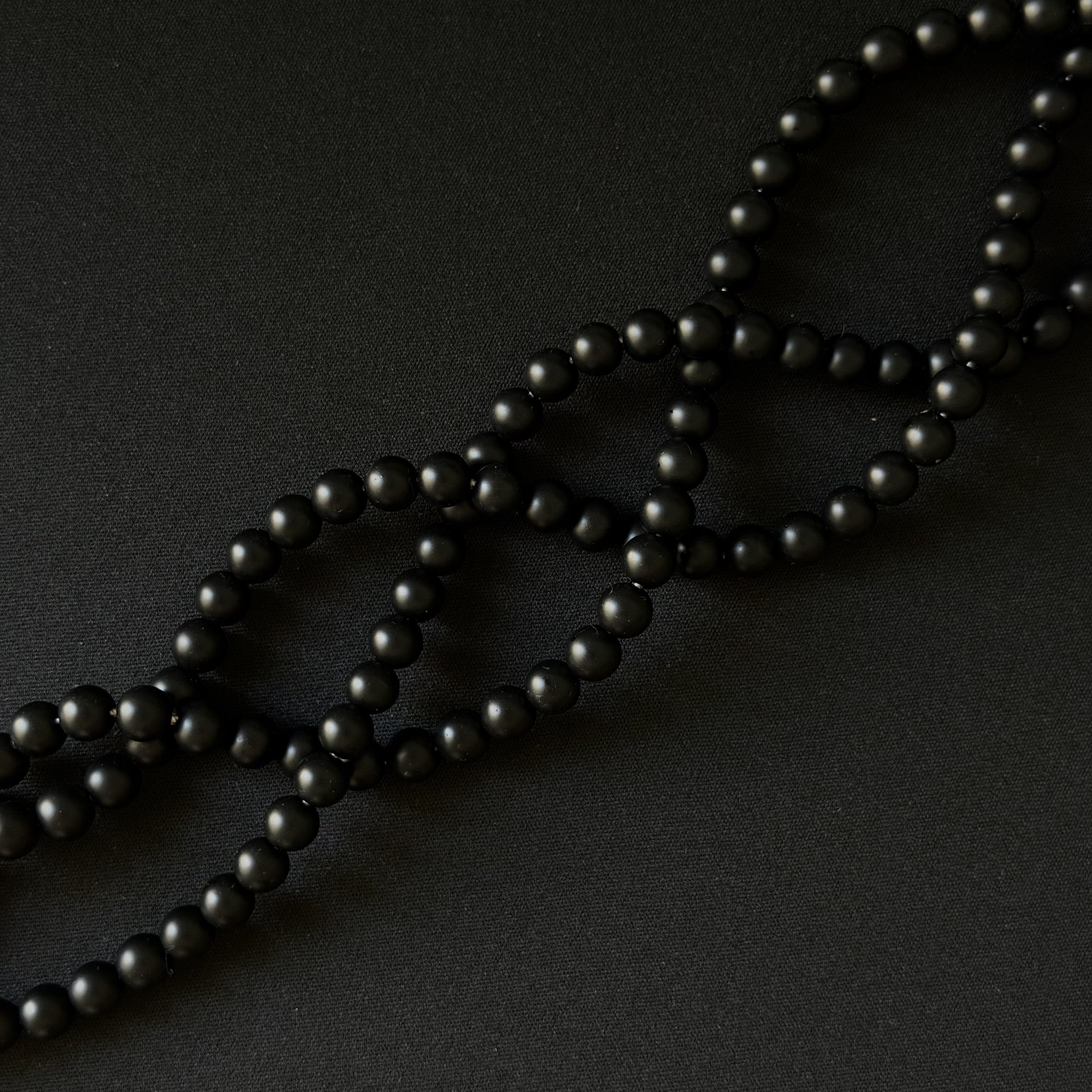 Black onyx matte round beads on a string for making necklace, arranged in a diagonal on a dark background. three strands