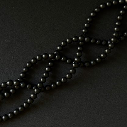 Black onyx matte round beads on a string for making necklace, arranged in a diagonal on a dark background. three strands
