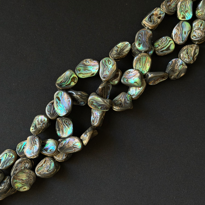 Abalone shell beads with a natural iridescent finish, arranged diagonally on a dark black background.