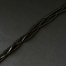 Black onyx tube beads arranged in a diagonal line on a dark textured background.