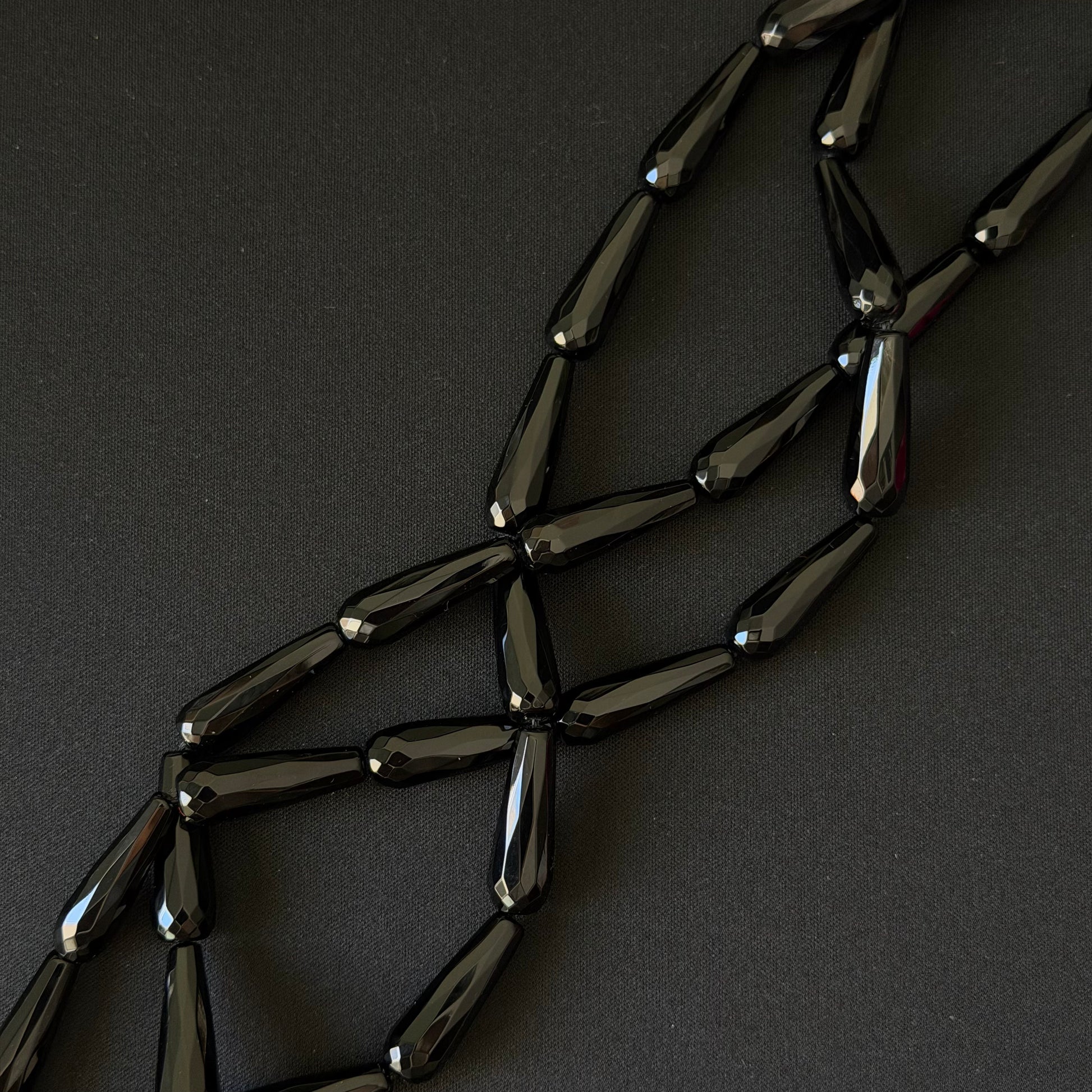 Black onyx teardrop beads on a string for necklace making, on a dark background