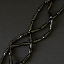 Black onyx teardrop beads on a string for necklace making, on a dark background