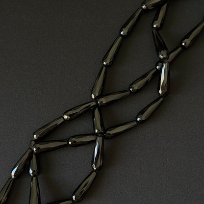 Black onyx teardrop beads on a string for necklace making, on a dark background