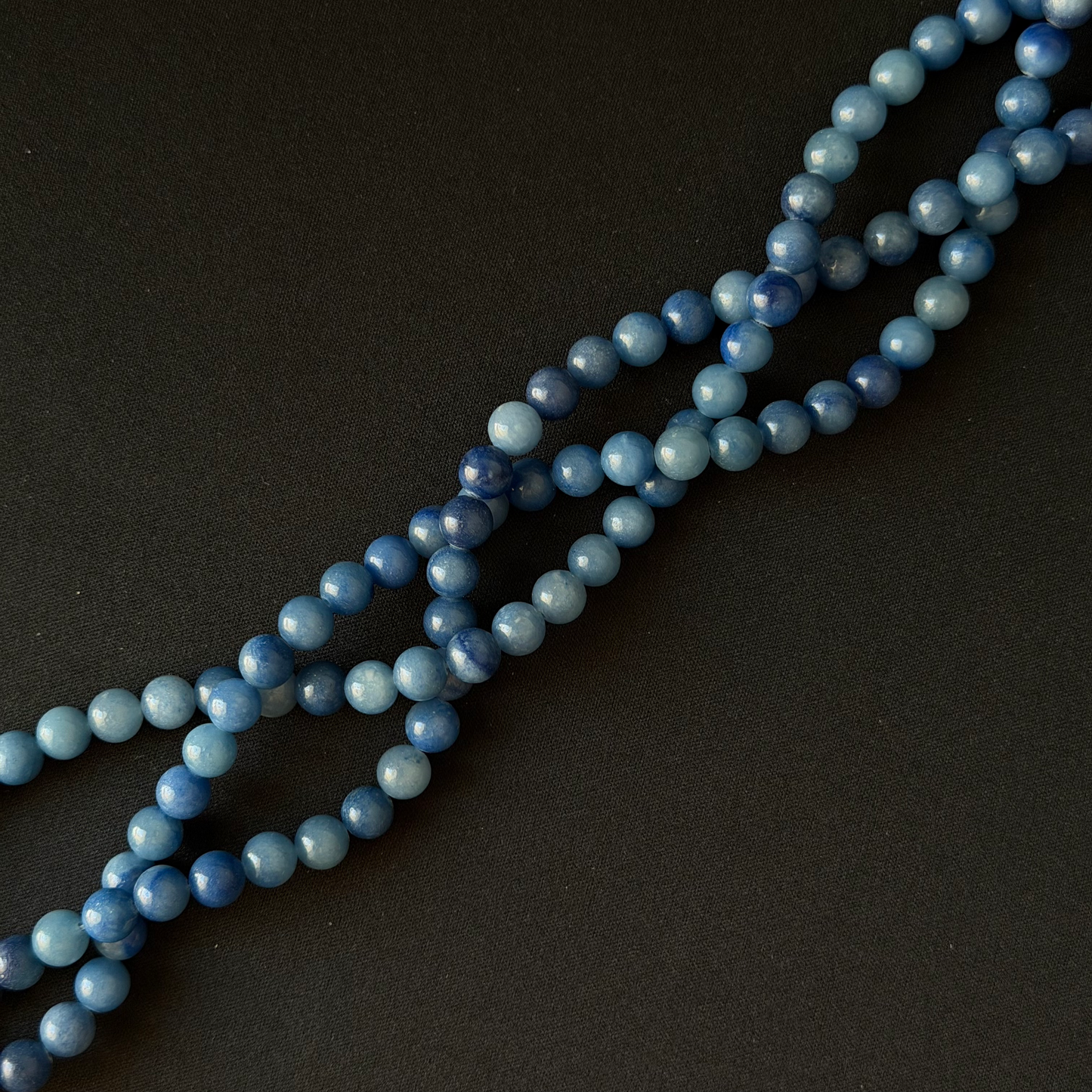 Blue aventurine bead strands, arranged diagonally on a dark textured background.