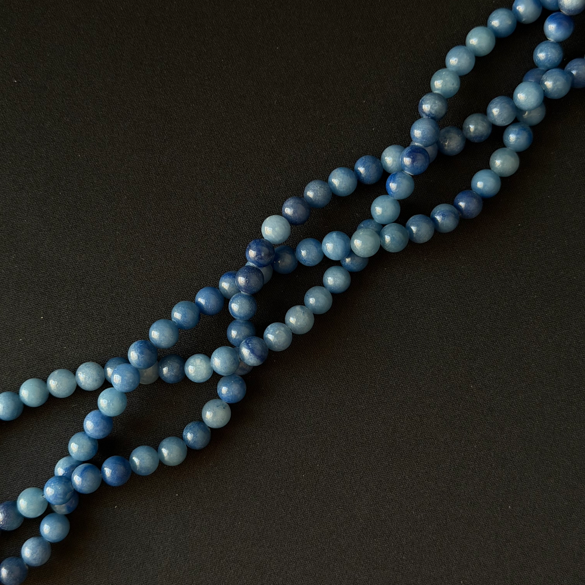 Blue aventurine bead strands, arranged diagonally on a dark textured background.
