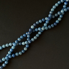 Blue aventurine bead strands, arranged diagonally on a dark textured background.