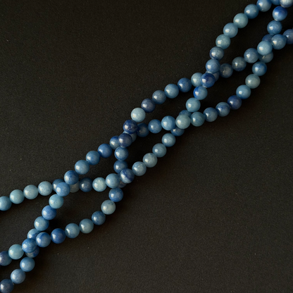 Blue aventurine bead strands, arranged diagonally on a dark textured background.