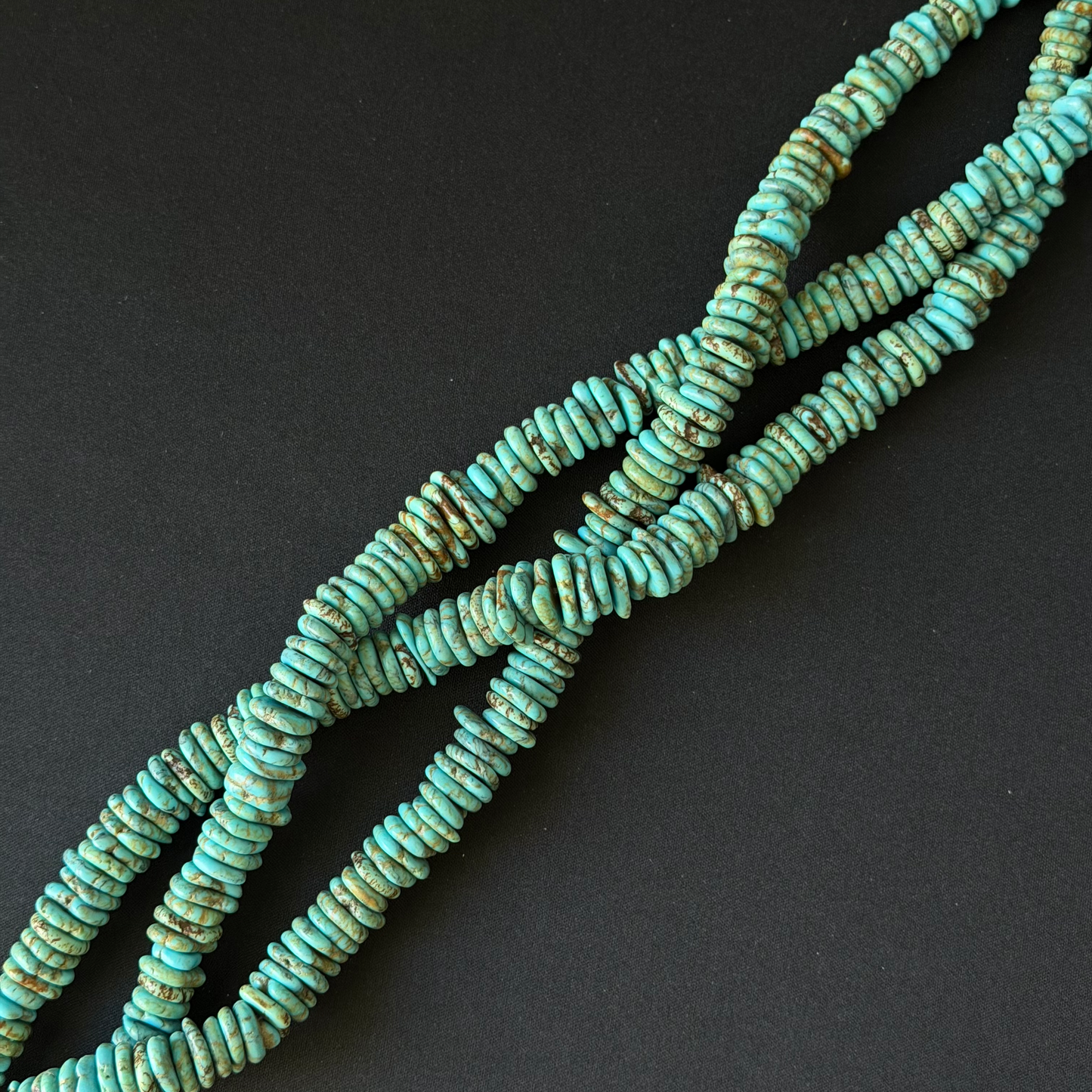 Turquoise stone chip beads with natural brown matrix, arranged in a loop on a dark gray background.