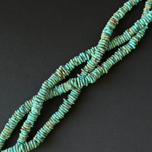 Turquoise stone chip beads with natural brown matrix, arranged in a loop on a dark gray background.