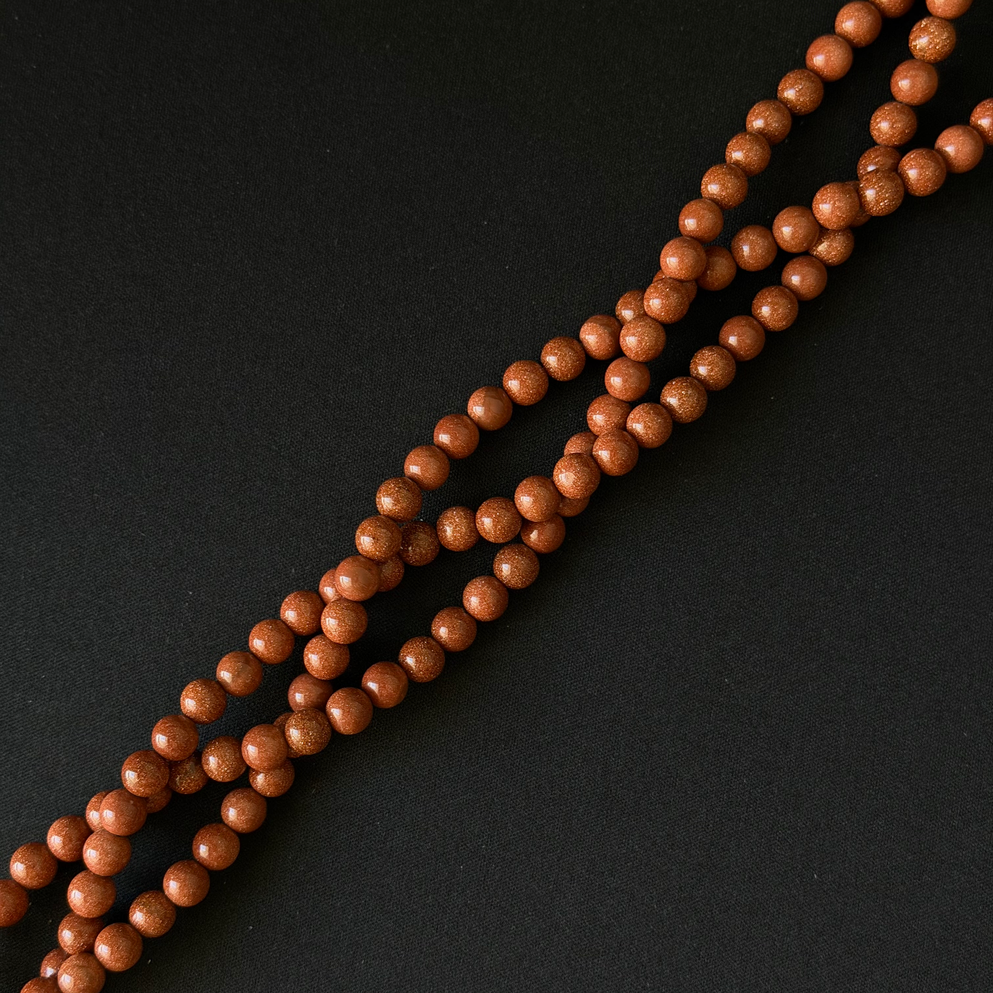 Three strands of small, polished gold sandstone beads arranged diagonally on a dark black background.