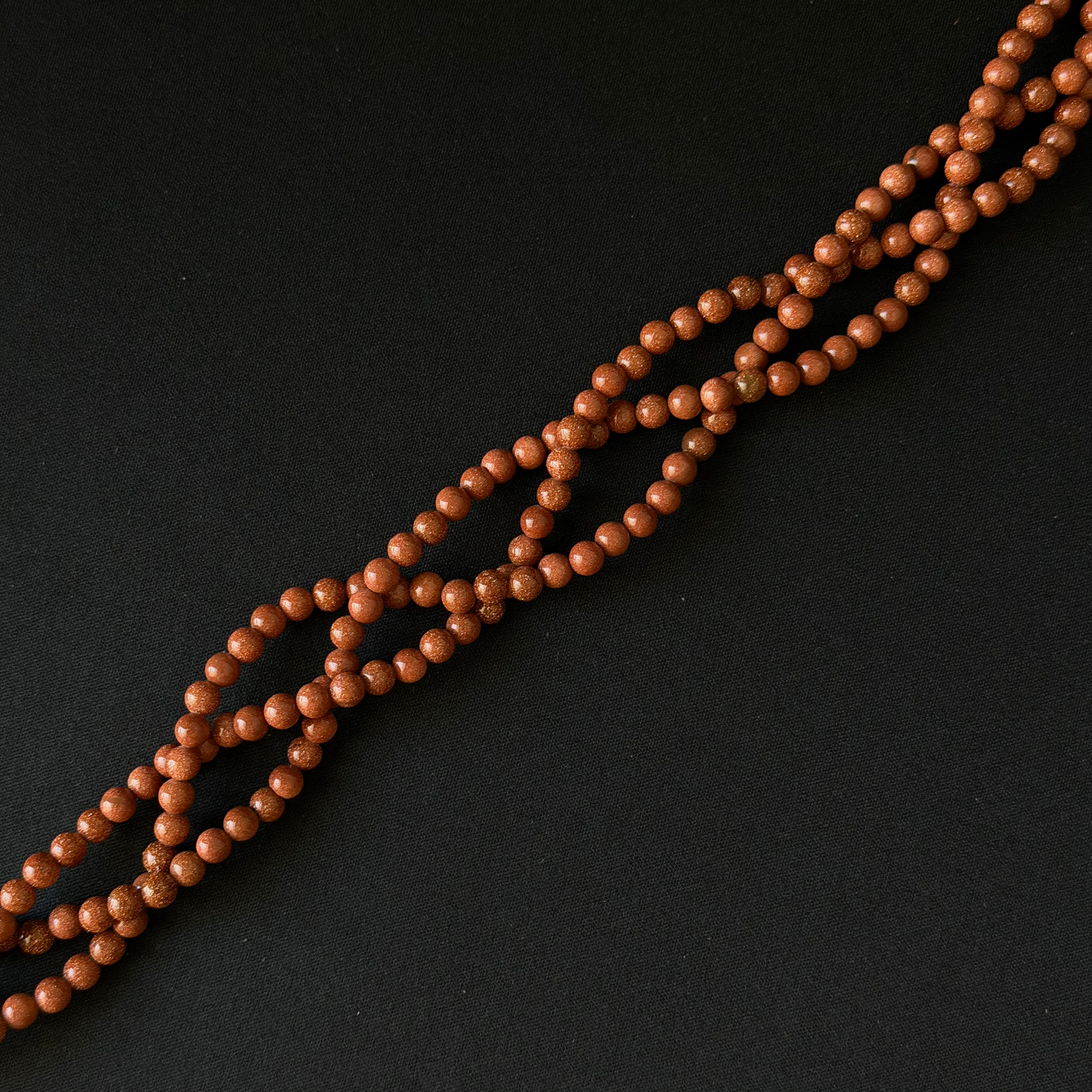 A strand of small, polished brown wooden beads arranged diagonally on a dark black background.
