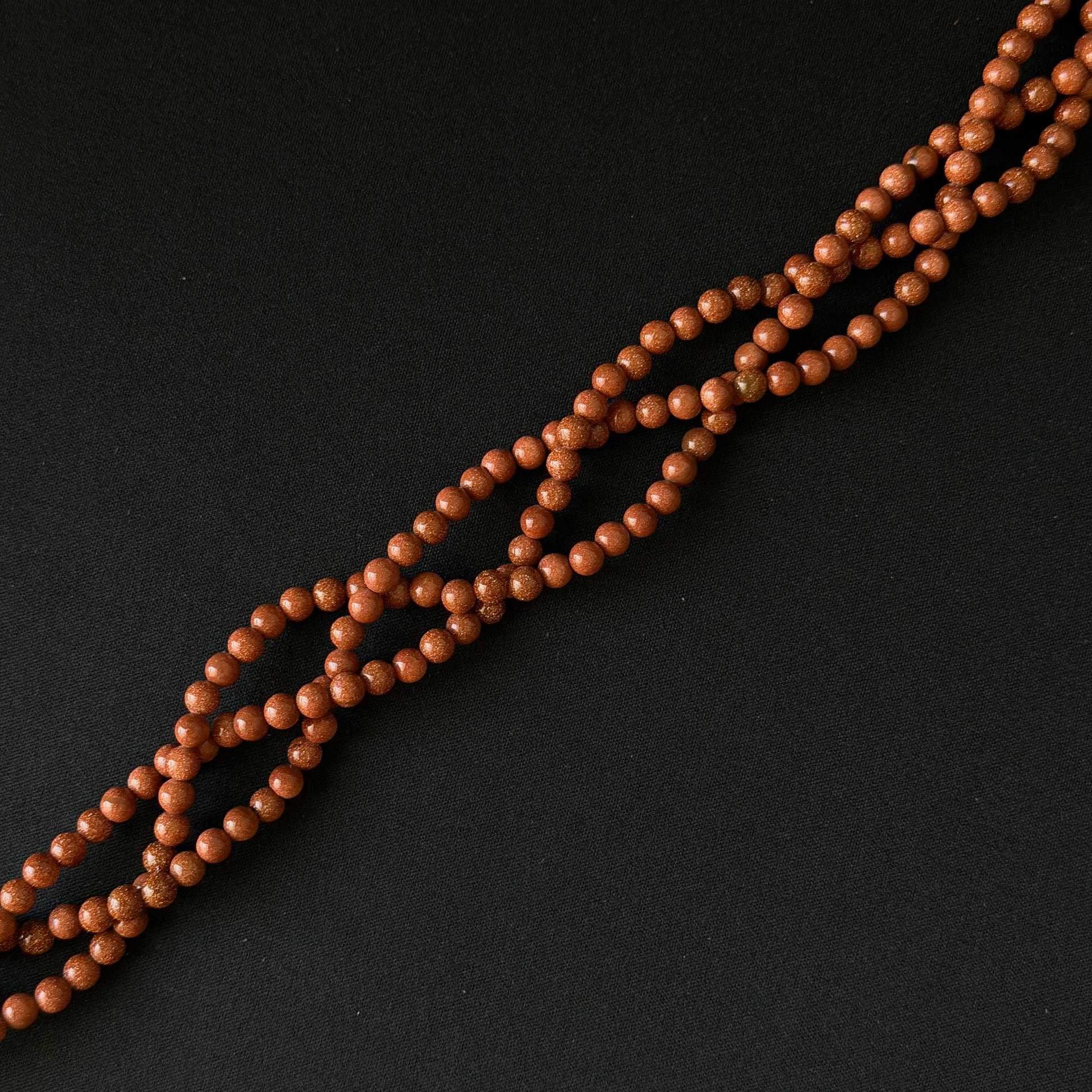 A strand of small, polished brown wooden beads arranged diagonally on a dark black background.