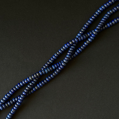 Three strands of small dark blue dyed lapis lazuli beads arranged diagonally on a dark gray background.