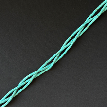 A strand of small turquoise-blue tube shape beads strung diagonally on a dark black background.