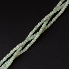 a close up of three pale green strands of rondelle beads. arranged at a diagonal on a black textured background.