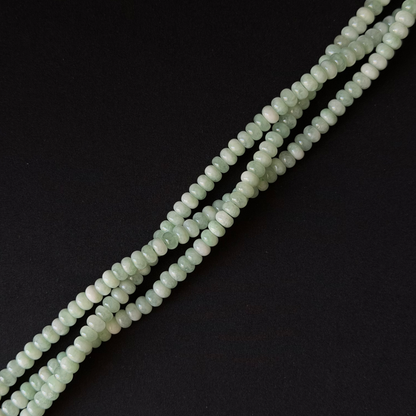 a close up of three pale green strands of rondelle beads. arranged at a diagonal on a black textured background.
