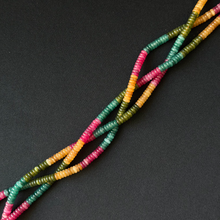 Multicolor beaded strands with alternating sections of teal green, pink, and yellow beads, arranged diagonally on a dark gray background.