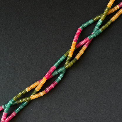 Multicolor beaded strands with alternating sections of teal green, pink, and yellow beads, arranged diagonally on a dark gray background.