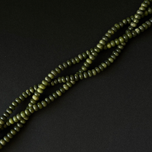 A close-up of olive green smooth rondelle beads strung on a cord, arranged diagonally on a dark black background.