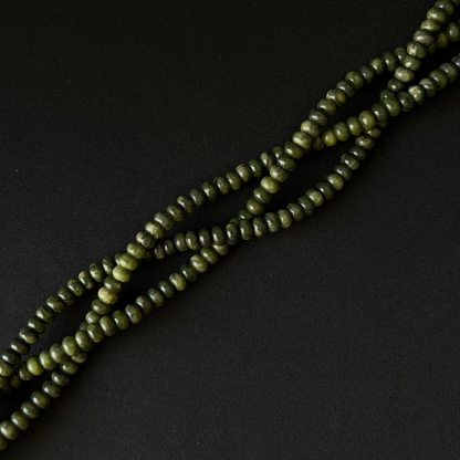 A close-up of olive green smooth rondelle beads strung on a cord, arranged diagonally on a dark black background.