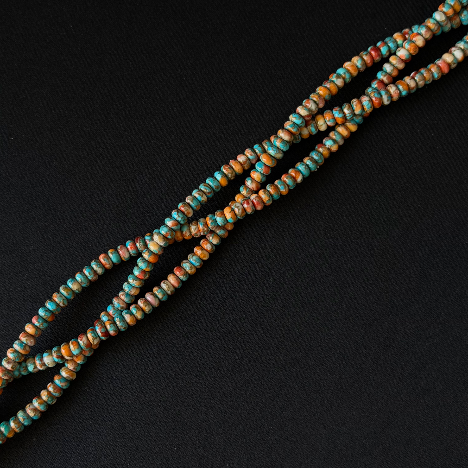 Multiple strands of spiny oyster small rondelle beads with a mottled turquoise, brown, and cream pattern, arranged diagonally on a solid black background.