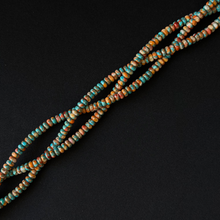 Multiple strands of spiny oyster small rondelle beads with a mottled turquoise, brown, and cream pattern, arranged diagonally on a solid black background.
