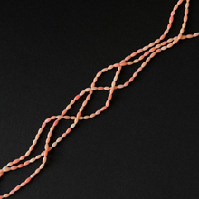 A strand of smooth bamboo coral peach-pink beads arranged diagonally on a solid black background.