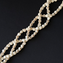 A strand of small skull-shaped beads in off-white with dark eye sockets, arranged diagonally on a solid black background.