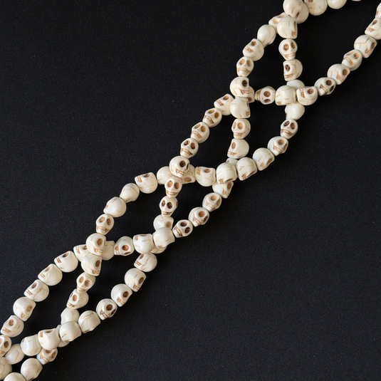 A strand of small skull-shaped beads in off-white with dark eye sockets, arranged diagonally on a solid black background.