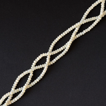 A strand of small, round, off-white beads arranged in a diagonal line on a solid black background.