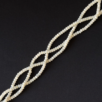 A strand of small, round, off-white beads arranged in a diagonal line on a solid black background.