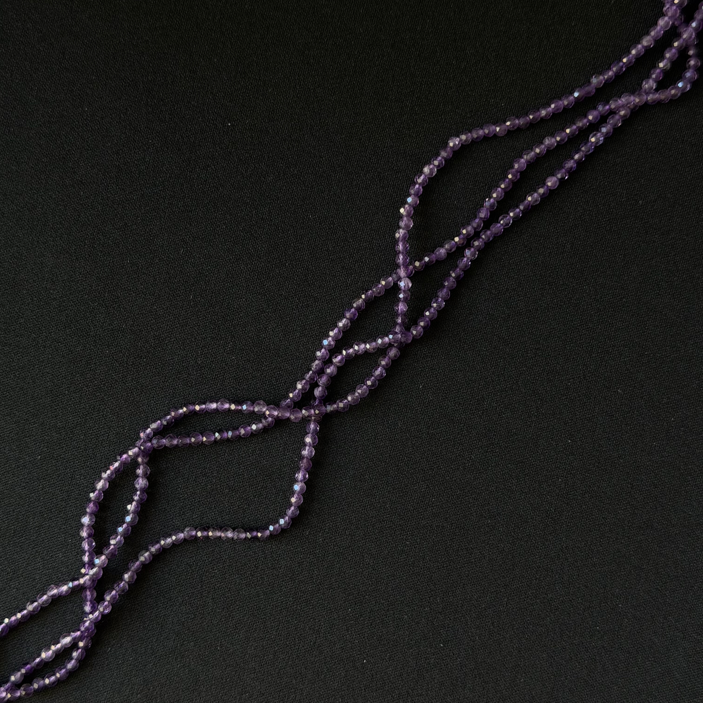Purple Amethyst beaded strands arranged diagonally on a dark black background.