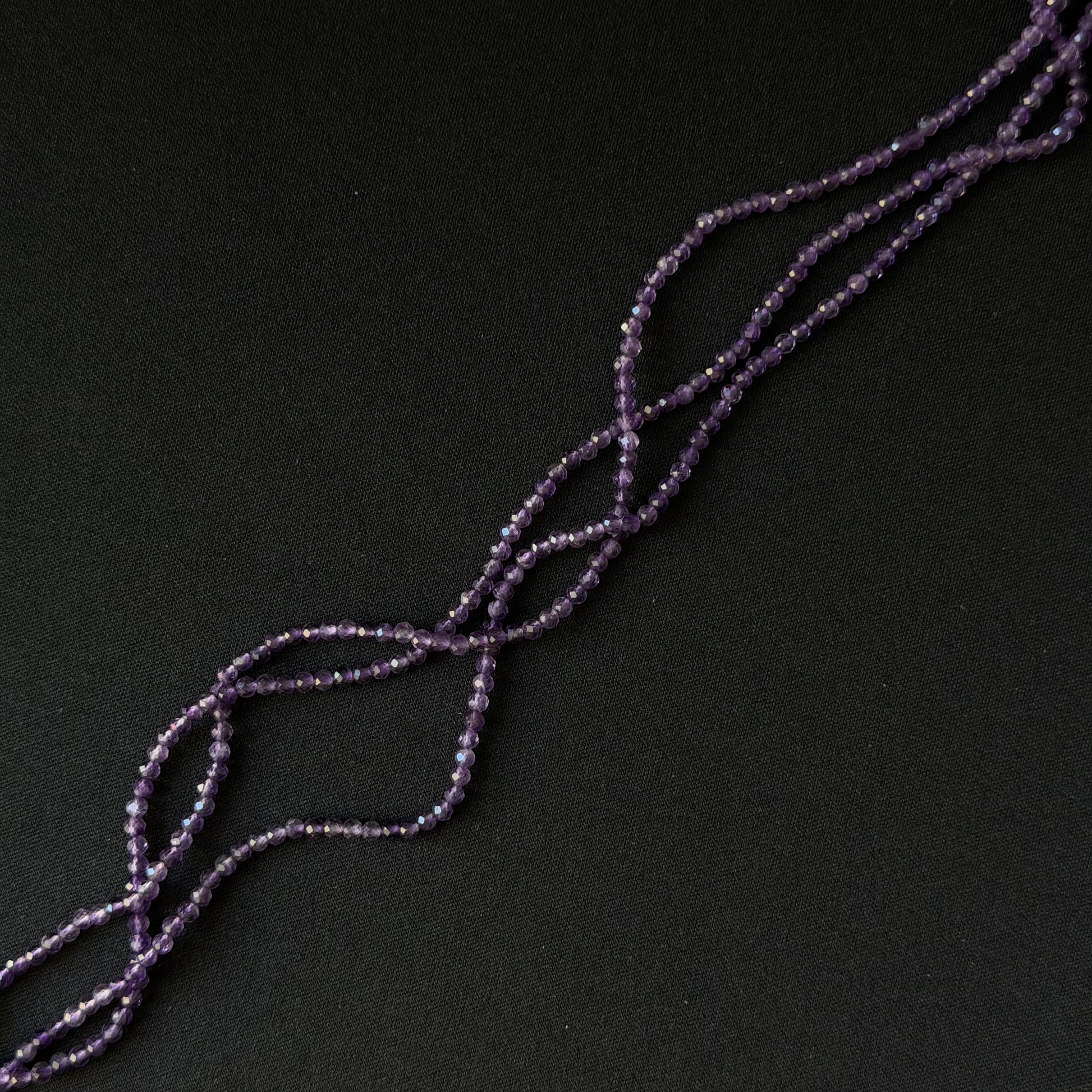 Purple Amethyst beaded strands arranged diagonally on a dark black background.