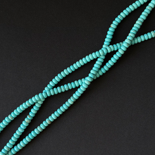 Turquoise-colored round beads strung on cords, arranged diagonally on a dark black background.