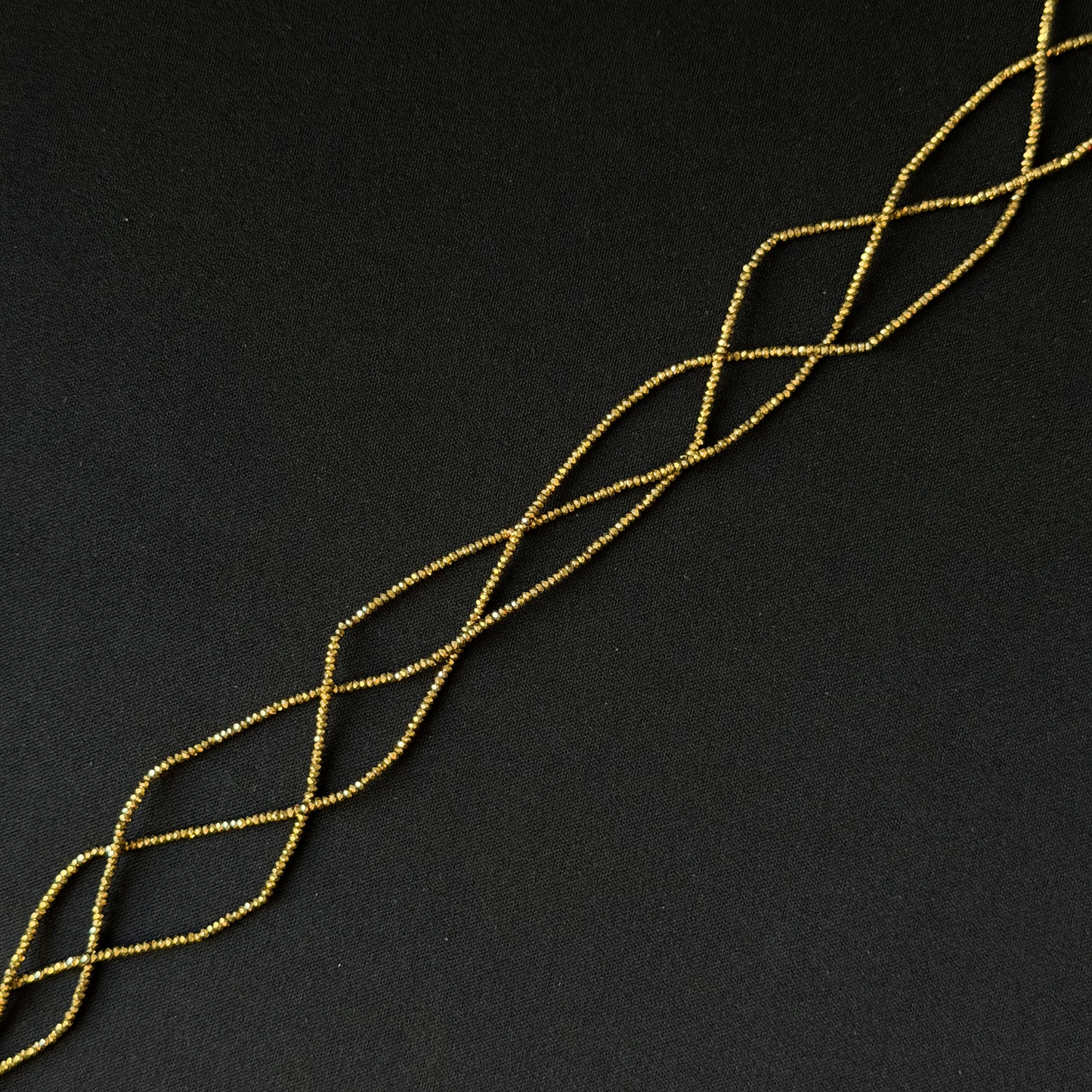 A close-up of a gold plated hematite beads on string arranged diagonally on a dark black background.