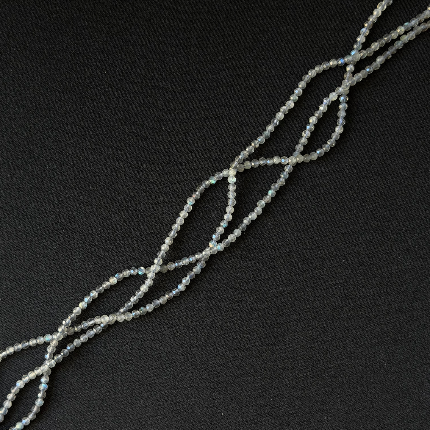 A strand of small iridescent labradorite faceted beads arranged in a loose spiral on a dark black background.
