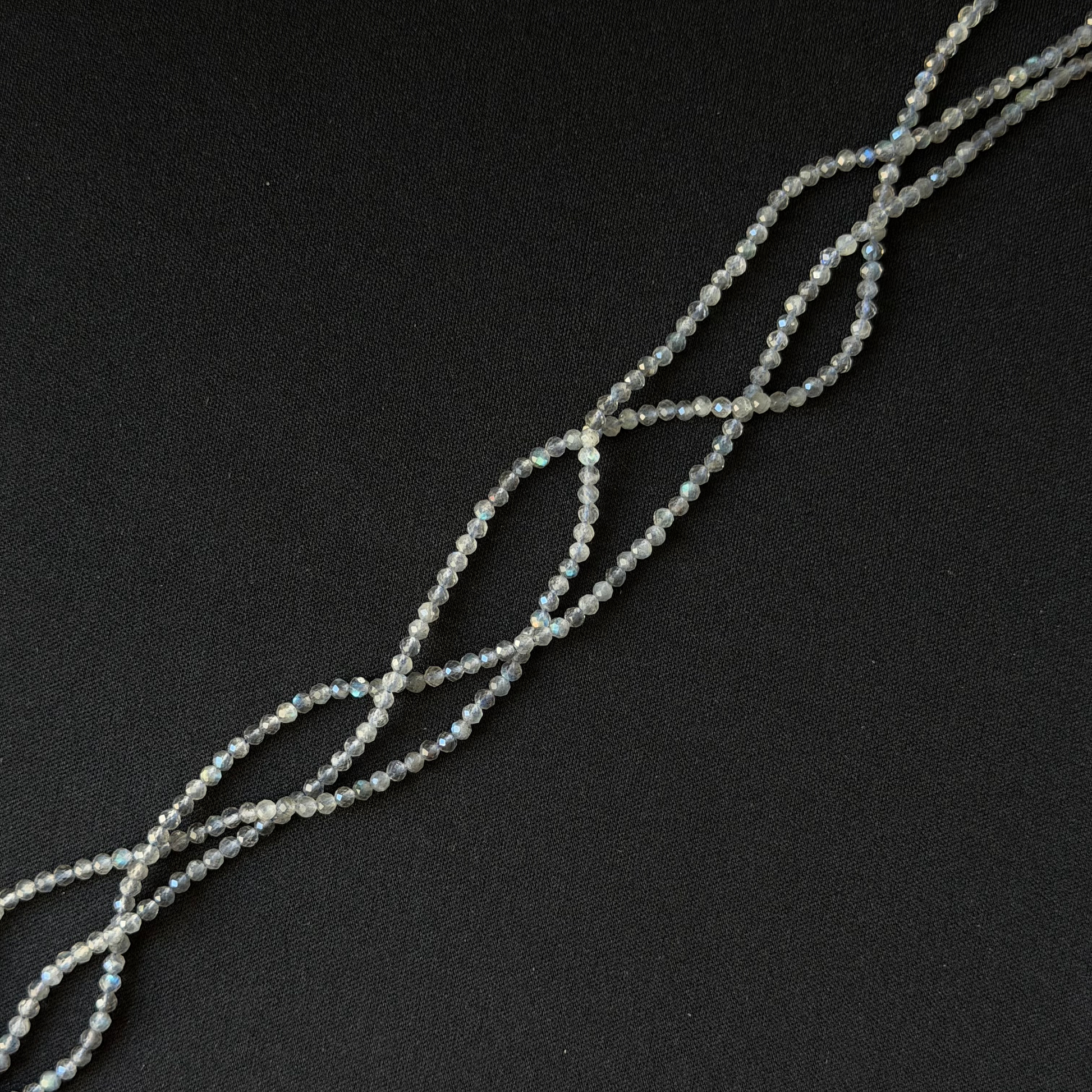 A strand of small iridescent labradorite faceted beads arranged in a loose spiral on a dark black background.