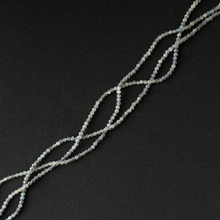 A strand of small iridescent labradorite faceted beads arranged in a loose spiral on a dark black background.