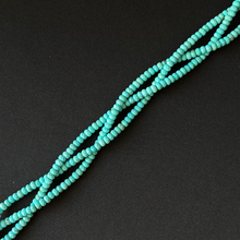 Turquoise beaded strands arranged diagonally on a dark textured background.
