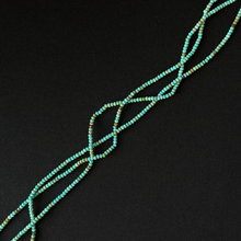 A close-up of a beaded strand or necklace made of small turquoise-blue beads with subtle multicolor flecks, arranged diagonally on a solid black background.