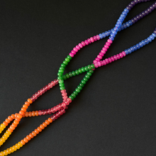A set of multi-strand beaded dyed jade arranged in a crisscross pattern on a dark black background. The necklaces feature translucent faceted beads in a rainbow gradient, transitioning from yellow and orange, through red and pink, to green, blue, and purple.