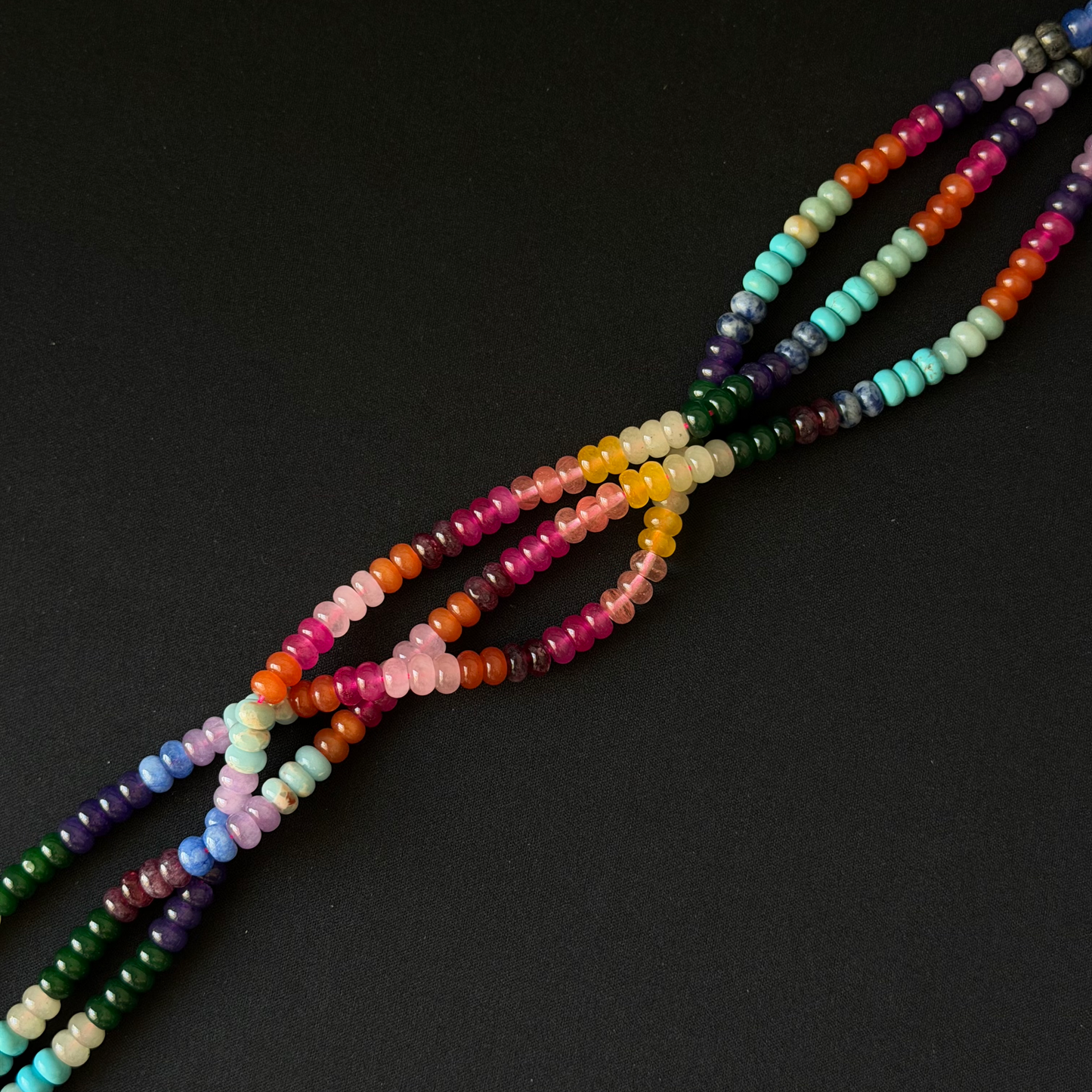 A set of multicolor beaded strands,gemstone beads, arranged diagonally on a solid black background.