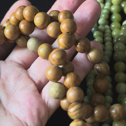 brown wood grain jasper beads in a close up video with beads in a persons hand. smooth round beads