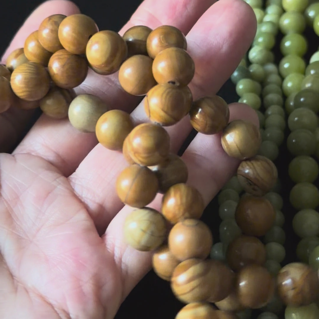brown wood grain jasper beads in a close up video with beads in a persons hand. smooth round beads