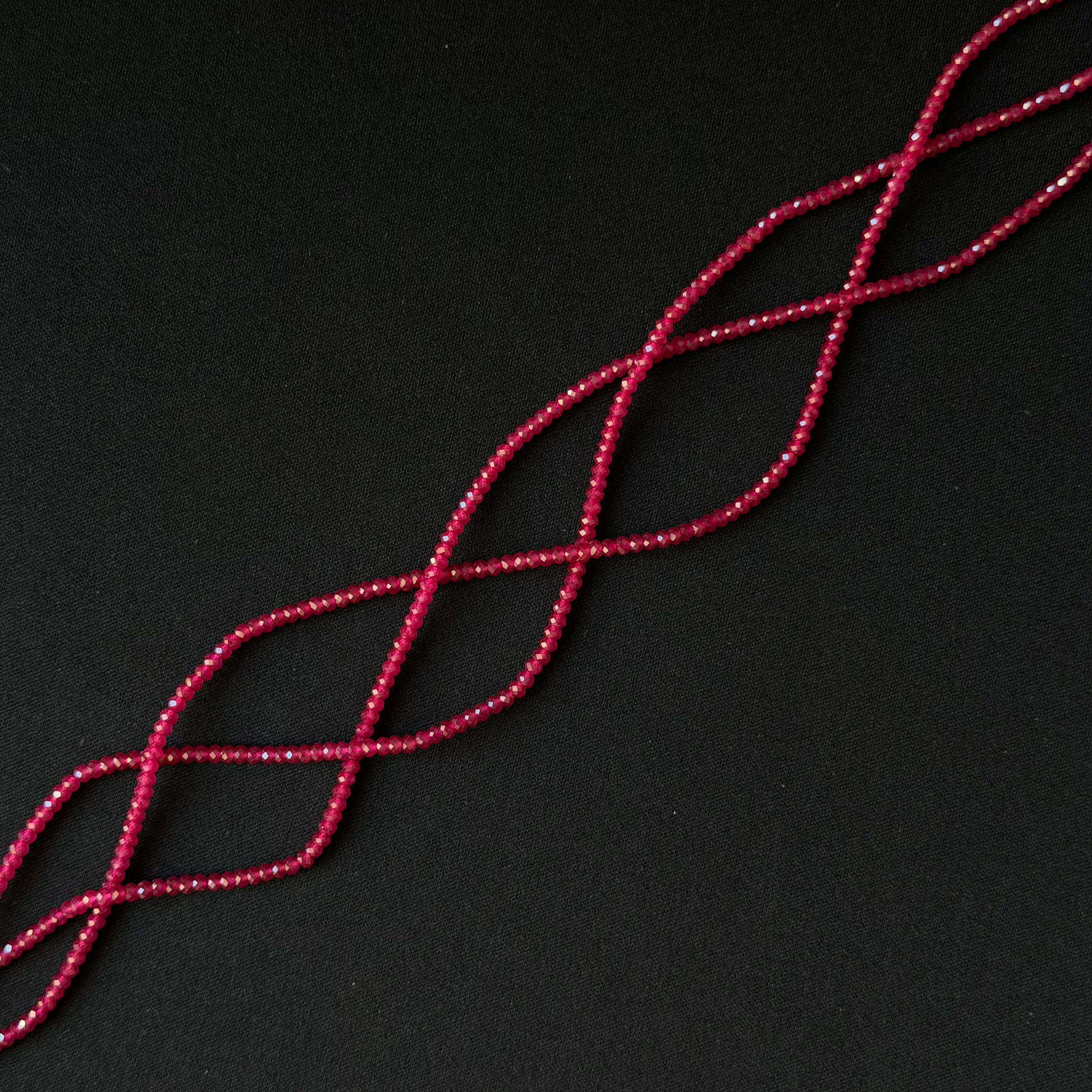 A close-up of a dark red dainty beads on a string arranged in a diagonal lattice pattern against a solid black background.