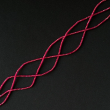 A close-up of a dark red dainty beads on a string arranged in a diagonal lattice pattern against a solid black background.