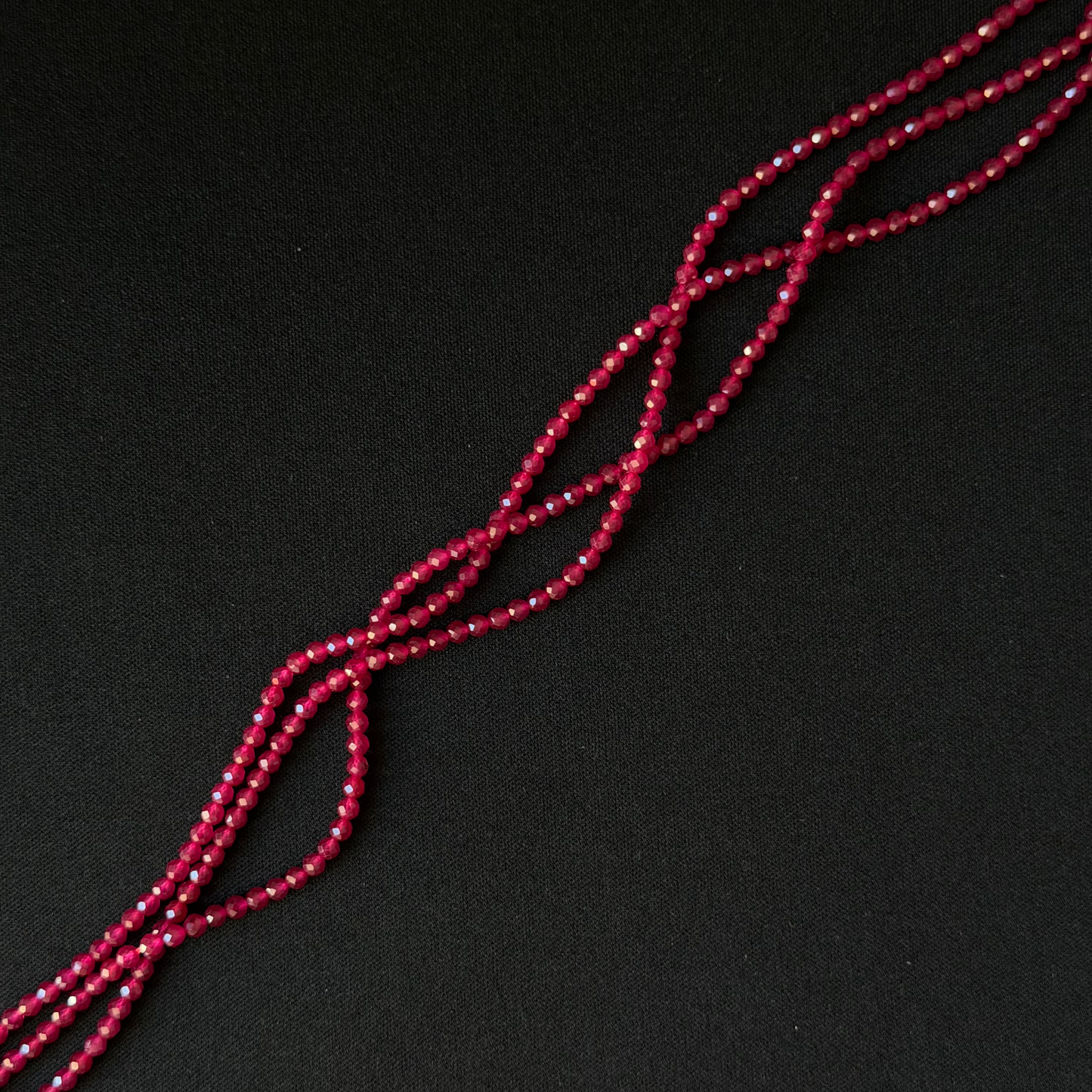 A close-up of a long strand of small faceted red beads arranged diagonally on a dark black background.